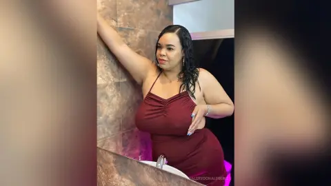 ValeryDonaldsons poses in a tight maroon dress, leaning against a brown tiled wall with one arm raised.