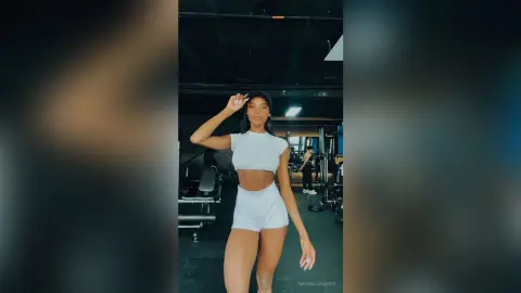 Fit woman in white crop top and shorts posing confidently in a modern gym setting.
