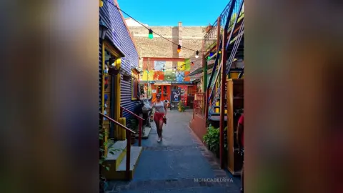 Stylish woman in red shorts walking through a colorful, vibrant narrow alleyway with festive string lights.