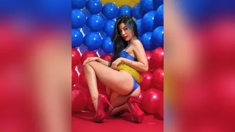 JessieLiu poses in a blue bodysuit and yellow mesh fabric, wearing red high heels against a background of blue and red balloons.