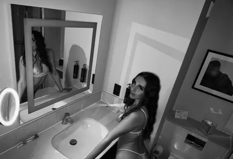 BrunetteBaddiex poses in a bathroom mirror wearing white lace lingerie.