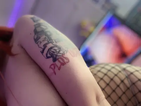 Close-up of a woman's tattooed arm and fishnet stockings in a dimly lit bedroom setting.