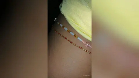 Close-up of a person wearing colorful beaded belly chains and a yellow top in a soft, summer aesthetic.