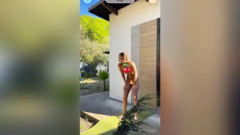 Fit woman in a red bikini stretching outdoors in a sunny garden setting.