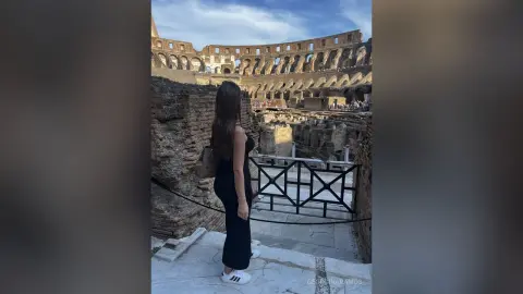 Woman in a black dress overlooking the ancient Roman Colosseum ruins under a clear blue sky.