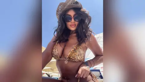 Stylish woman in tiger print bikini and cowboy hat posing under a sunny blue sky at a summer beach resort.