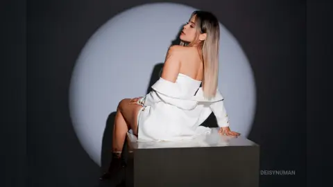 Elegant woman in a white off-the-shoulder blouse sitting against a minimalist circular spotlight background.
