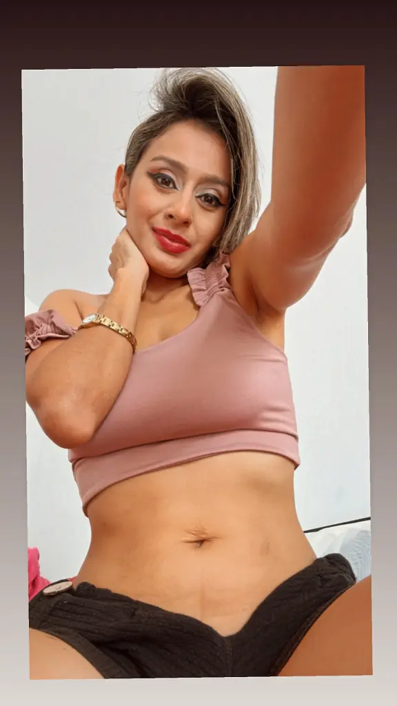 squiter29 poses in a blue bikini top and black bottoms, showing her cleavage and midriff against a patterned background.
