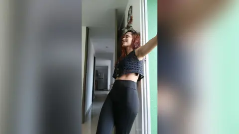 AmelieLautrec stands in a hallway wearing a black lace crop top and tight black leggings, showing her midriff and side profile.