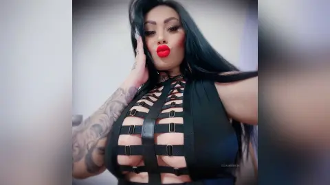 DeeaAnderson poses in a black cut-out bodysuit that exposes her breasts, running her hand up her face.