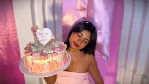 Young woman in a pink strapless top holding a celebratory pink cake for International Women's Day.