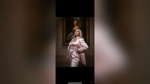 Elegant woman in a blush pink satin suit posing in a moody art gallery setting.