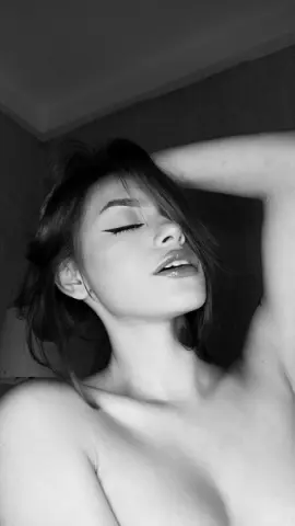 Close-up black and white portrait of a young woman with eyes closed in a moody, intimate indoor setting.