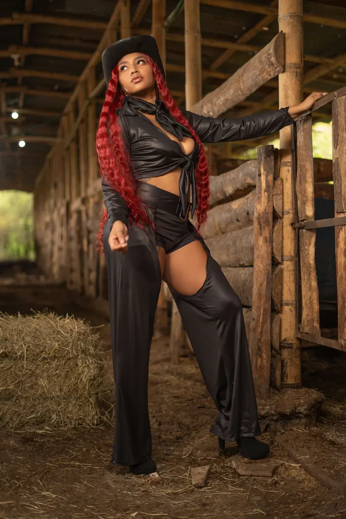 lindsayhoffman19 poses in a black top and matching necktie, showing off her long red hair against a soft, natural outdoor background.