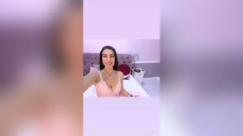 Smiling woman in a pink lace camisole relaxing in a bright, modern bedroom.