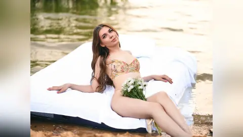 Young woman in floral bikini relaxing on a white floating mattress in a calm lake at sunset.