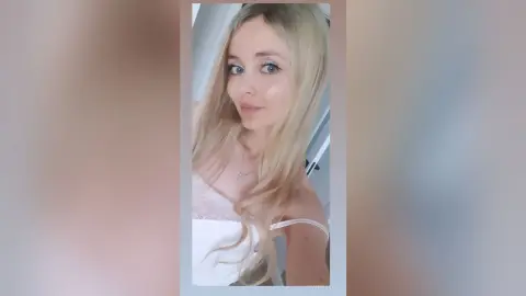 DianeDavies poses with her long blonde hair down, wearing a white lace camisole or slip top.