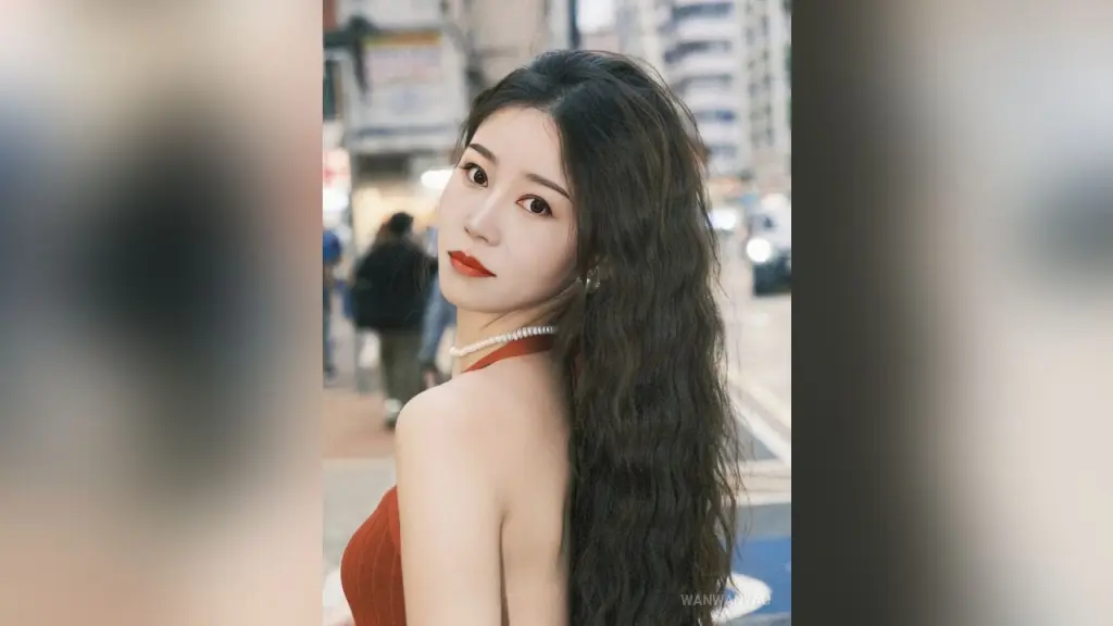 WanwanYao — Young woman with long wavy hair wearing a red dress and pearl necklace in a bright urban street setting.