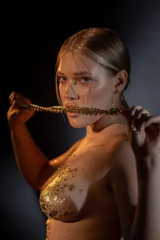 Glamorous woman with gold glitter body art and wet hair posing against a dark studio background.