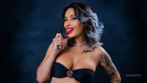 Glamorous woman in a black bandeau top and pearl necklace sticking her tongue out against a dark background.