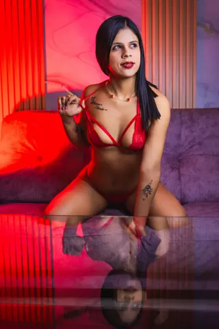 Young woman in red lingerie sitting on a purple sofa in a moody, red-lit room.