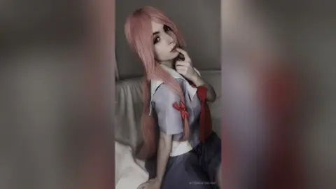 Cosplayer with long pink hair wearing a school uniform sitting on a bed in a soft, dreamy mood.