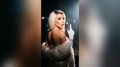 Glamorous blonde singer in a white fur stole holding a vintage microphone on a dark stage.