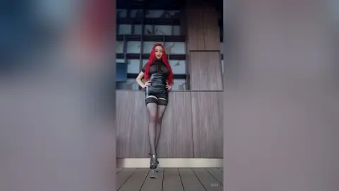 Red-haired woman in a sleek black mini dress posing confidently in a modern wood-paneled interior.