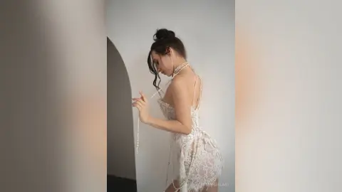 StacyHarland — Elegant woman in a white lace backless dress with long pearl strands in a minimalist studio setting.