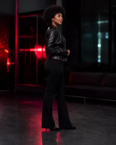 KylieDecks — KylieDecks stands in a dark room wearing a black leather jacket and tight black flared pants.