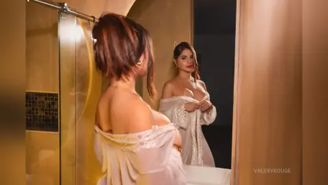 ValeryRouge looks into a mirror wearing a white off-the-shoulder lace top, showing her bare shoulders and neck.
