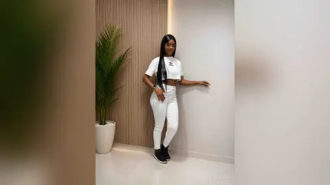 Stylish woman in white Adidas crop top and skinny jeans posing in a modern minimalist room with a green plant.