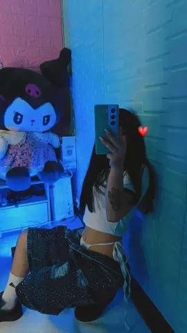 Young woman in casual white crop top and denim shorts sitting in a blue lit room with a large plush toy.