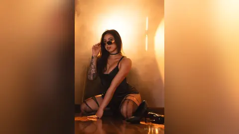 MilaWillow poses in a black lace bodysuit and sunglasses, kneeling on the floor in warm lighting.