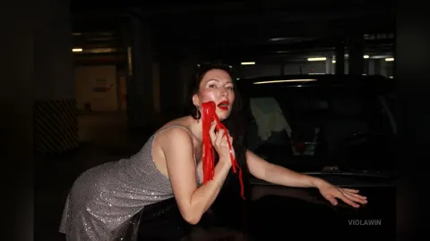 ViolaWin — ViolaWin leans against a black car in a dark garage wearing a sparkly silver dress while red liquid drips from her mouth.