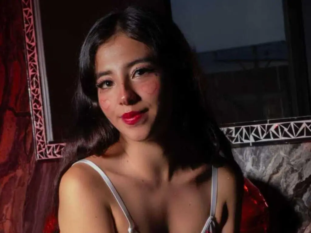 Young woman with dark hair and red lipstick in a moody, dimly lit indoor setting.