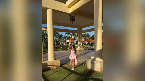 Young woman in a pink mini dress standing on a sunny patio overlooking tropical palm trees.