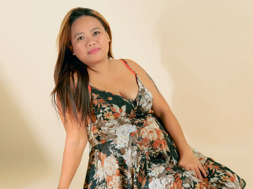 Smiling woman in a floral summer sundress posing against a neutral beige studio background.