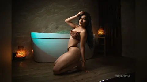 Elegant woman in a brown bikini posing in a moody, dimly lit bathroom with warm lantern lighting.