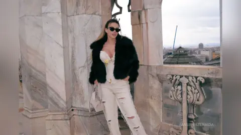 Stylish woman in white corset and jeans with black faux fur coat posing on a luxury marble balcony.
