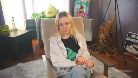 Blonde woman in a white shirt and black t-shirt sitting relaxed in a modern living room setting.