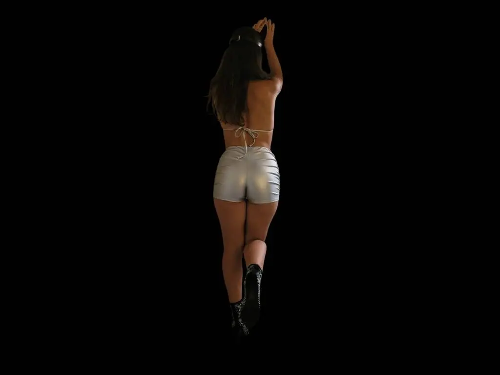 Woman in silver metallic shorts and black boots posing against a black background in a sleek, modern style.