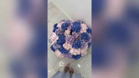 Elegant round hydrangea floral arrangement in shades of blue, purple, and pink on a marble floor.