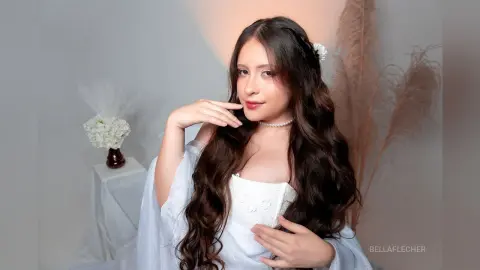 Young woman in a white lace corset and flowing robe posing elegantly in a soft, dreamy studio setting.