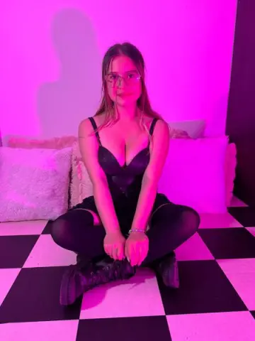 Young woman in a black bodysuit sitting on a checkered floor under moody pink lighting.