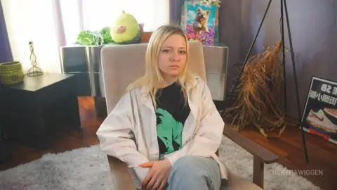 Blonde woman in a white shirt and jeans sitting in a cozy living room with a relaxed, calm mood.