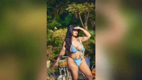 Curvy woman in a blue striped bikini relaxing in a lush tropical garden setting.