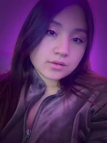 MiaHarveyyy looks into the camera wearing a grey zip-up top with her long dark hair down.