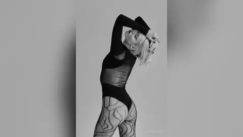 Elegant woman in a black long-sleeve bodysuit and patterned tights posing against a minimalist grey background.