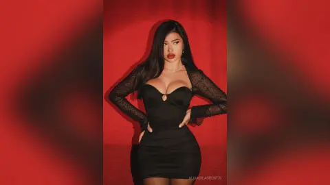 Glamorous woman in a black long-sleeve lace dress posing against a bold red background.